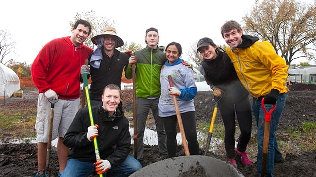 Seven smiling Kellogg Cares Day volunteers standing in a field holding shovels